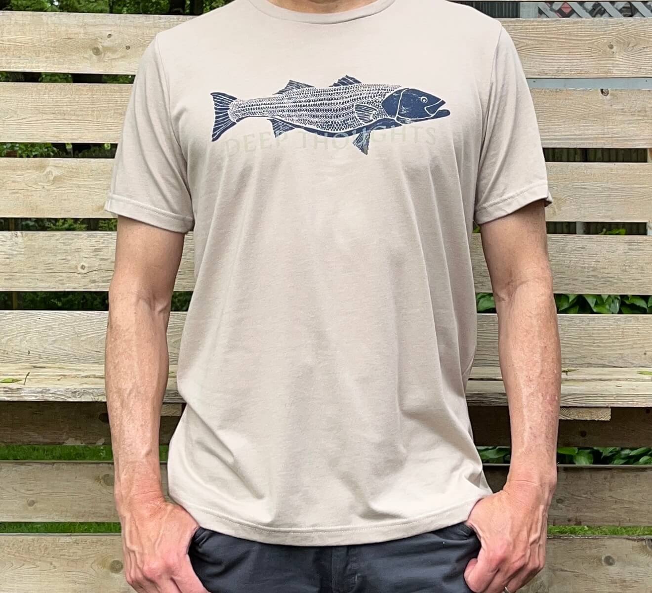 Man wearing heather tan t-shirt with navy blue striped bass illustration and faded DEEP THOUGHTS text