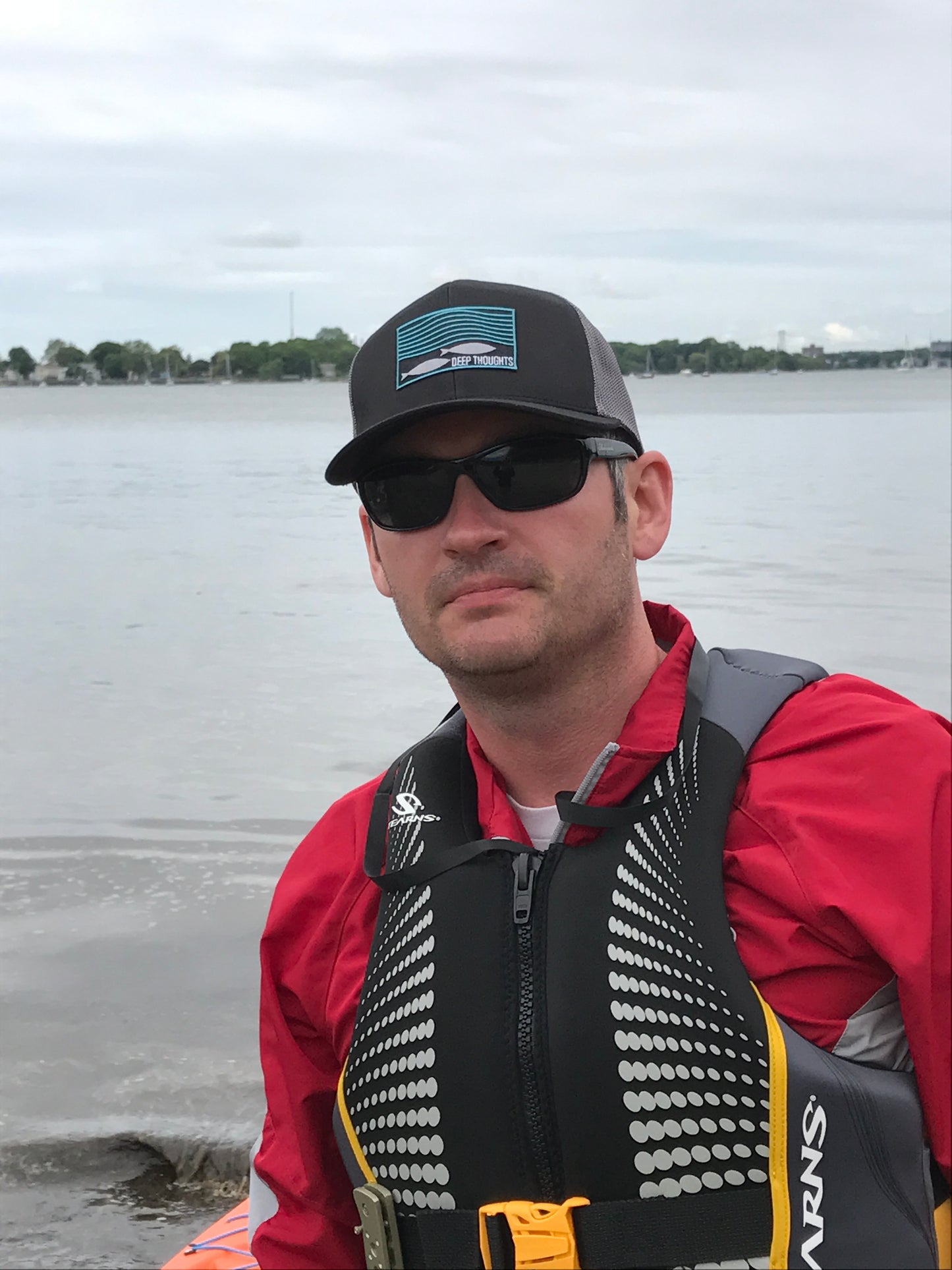 man wearing black and charcoal trucker hat with rectangular embroidered patch showing fish under wavy ocean currents