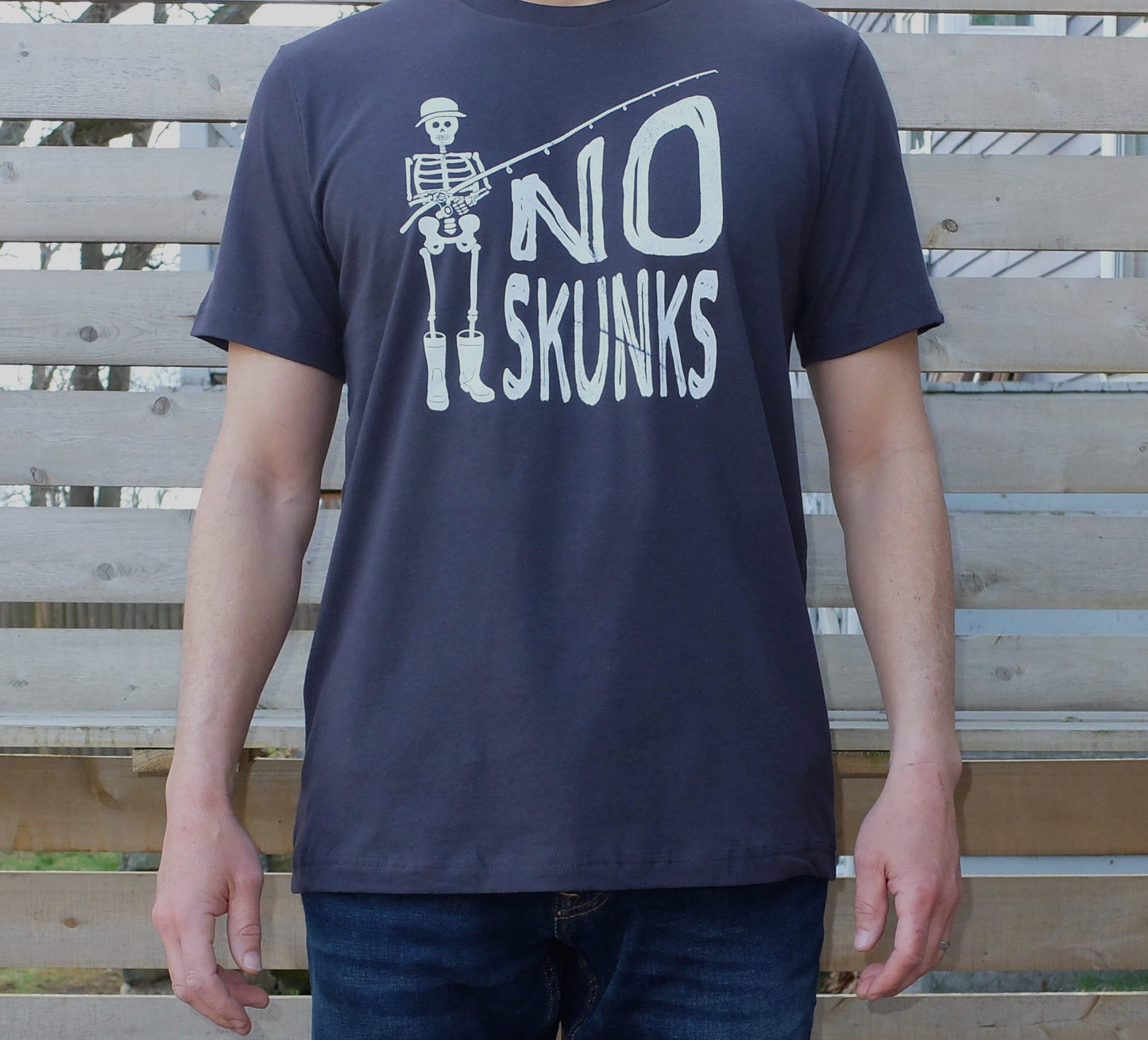 man wearing dark grey cotton t-shirt with white skeleton fisherman graphic and No Skunks text