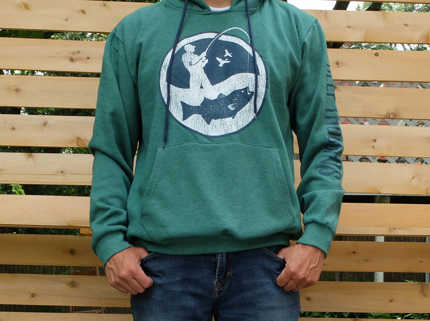 man wearing heather green hoodie with large round navy and white surf fisherman graphic