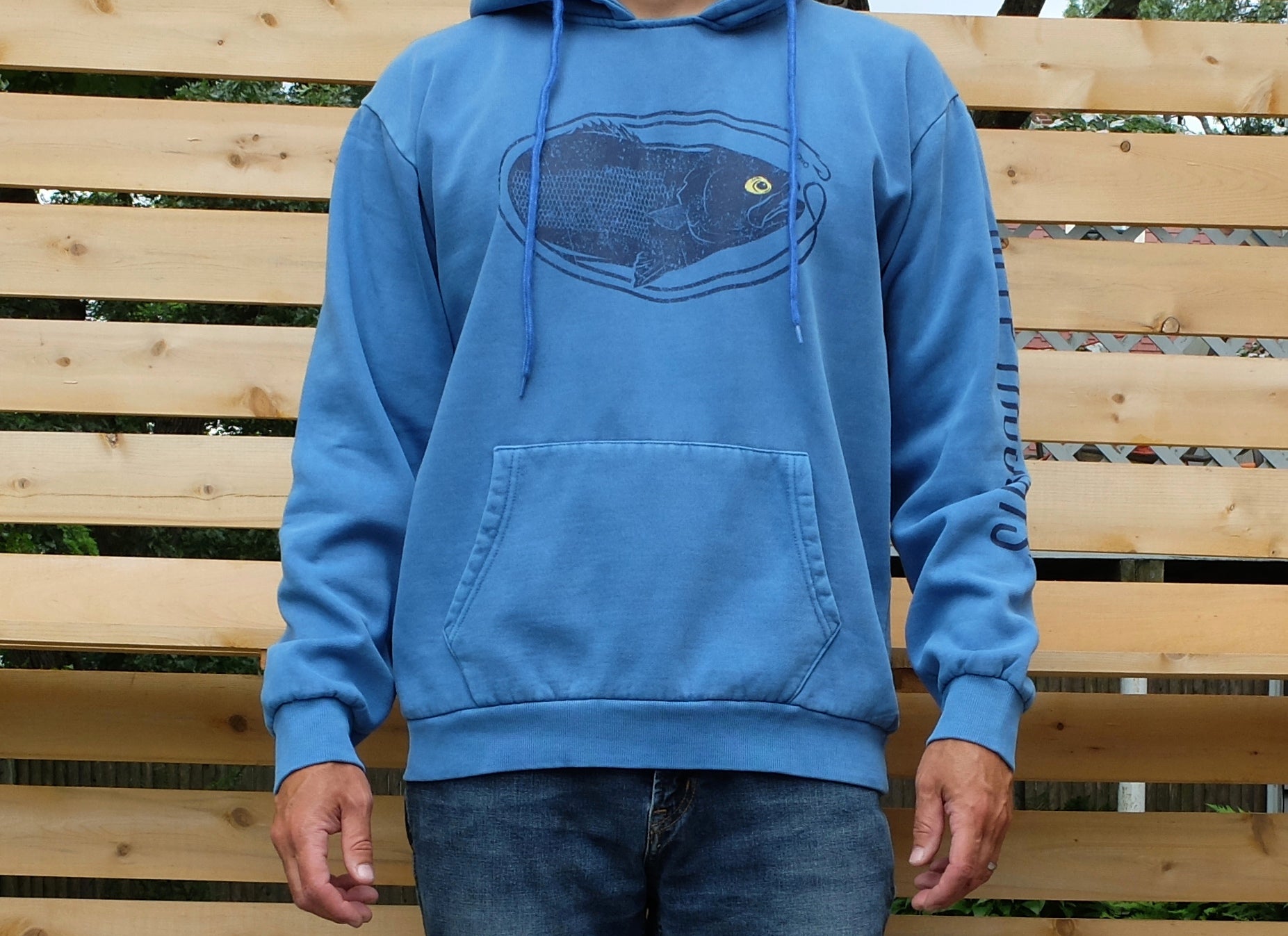 man wearing washed blue hoodie with oval-shaped dark blue vintage style bluefish fishing graphic