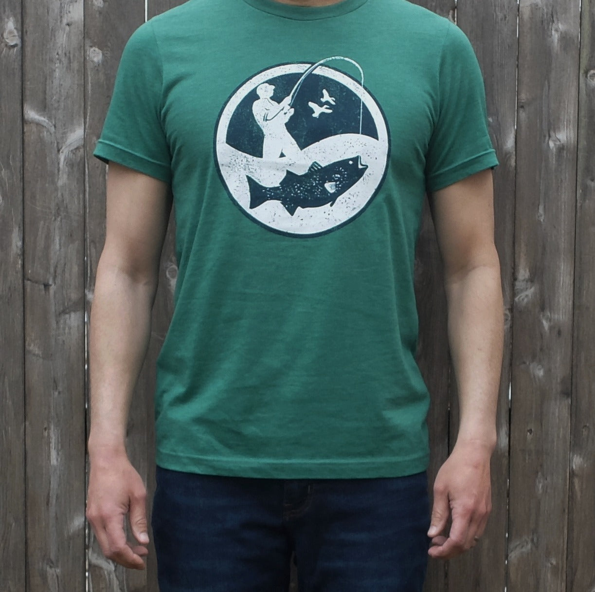 man wearing heather green t-shirt with round white and navy surf fisherman logo