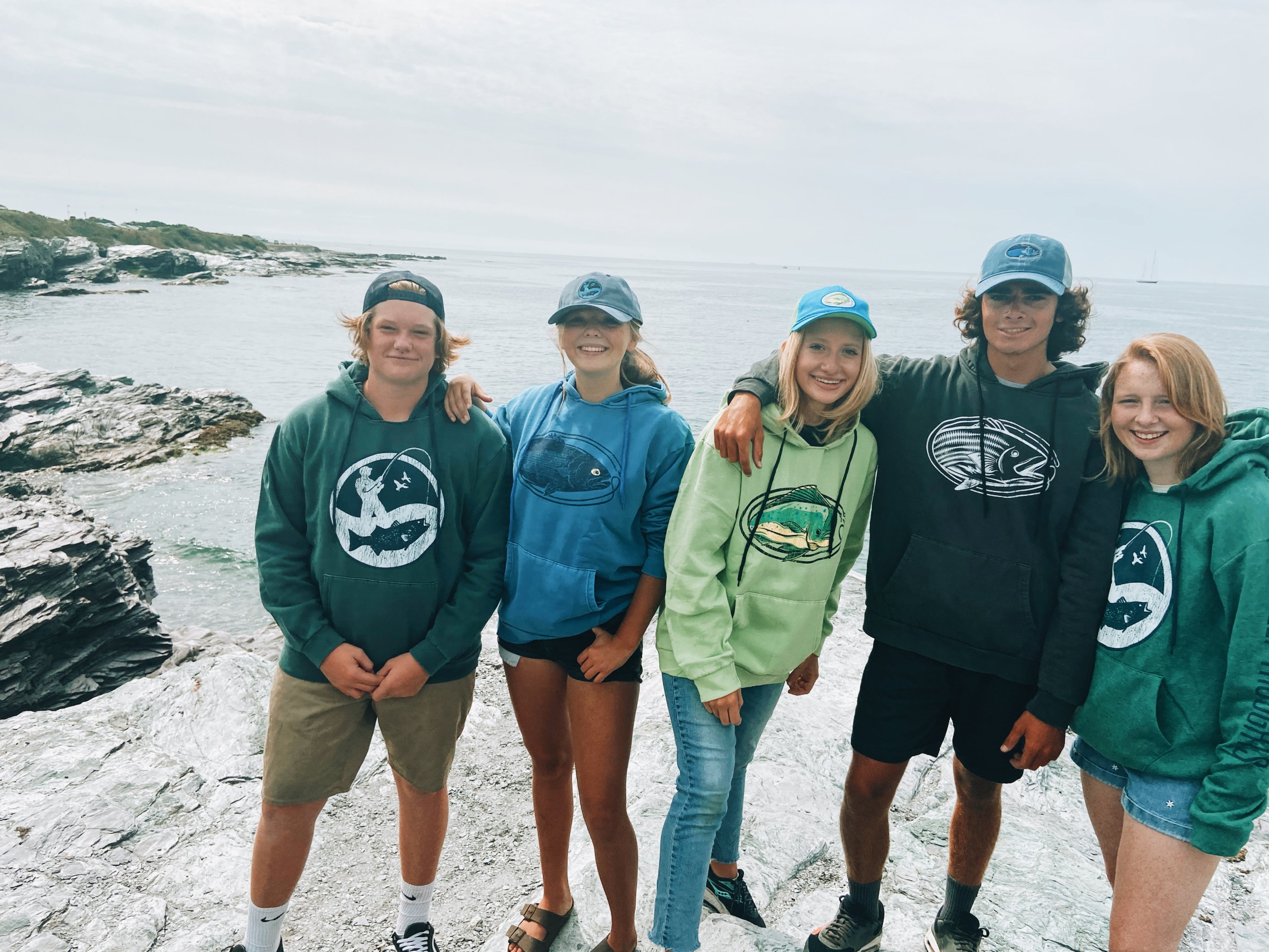 friends wearing Deep Thoughts Designs fishing hats and hoodies at rocky coastline