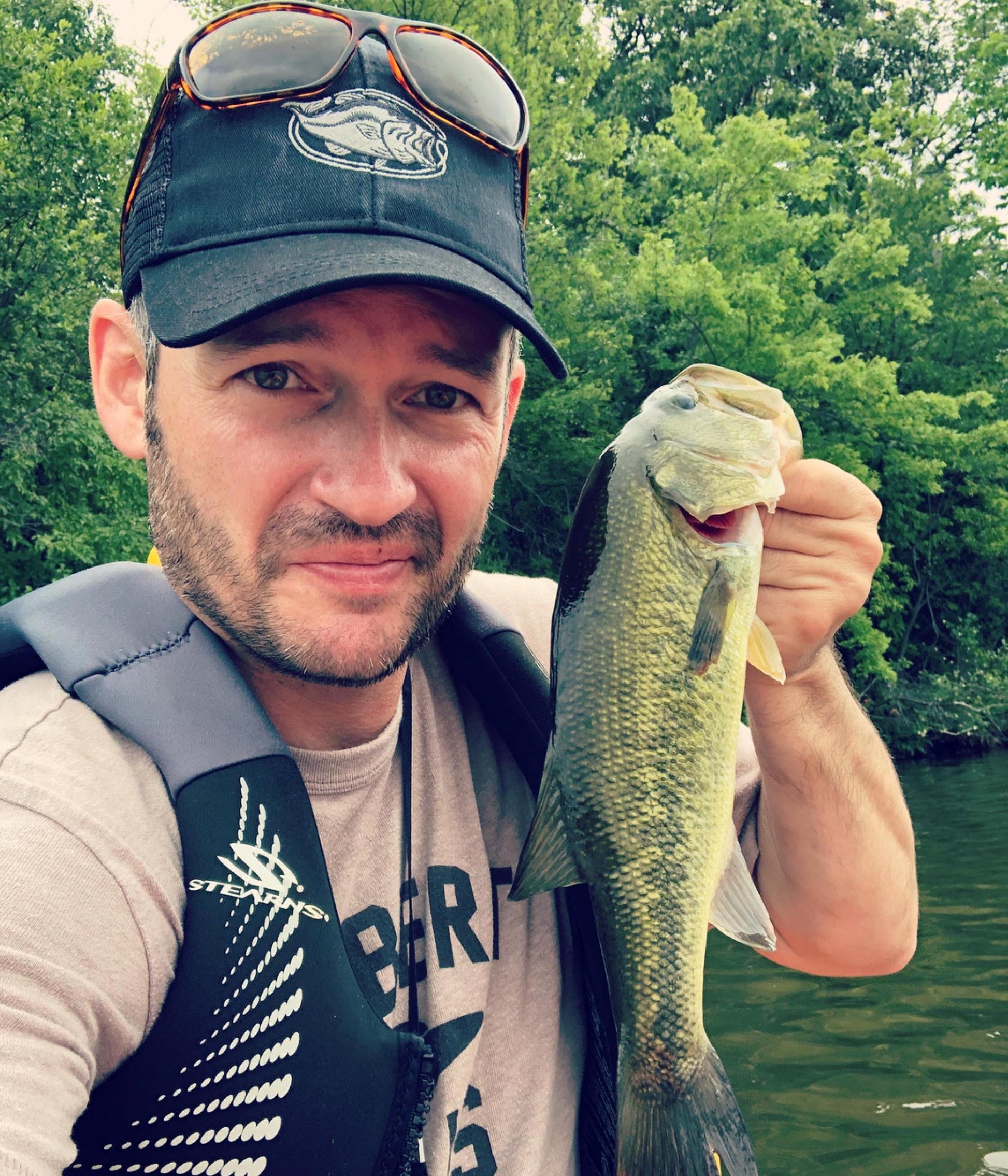 fisherman wearing black trucker hat with pewter grey embroidered largemouth bass decoration