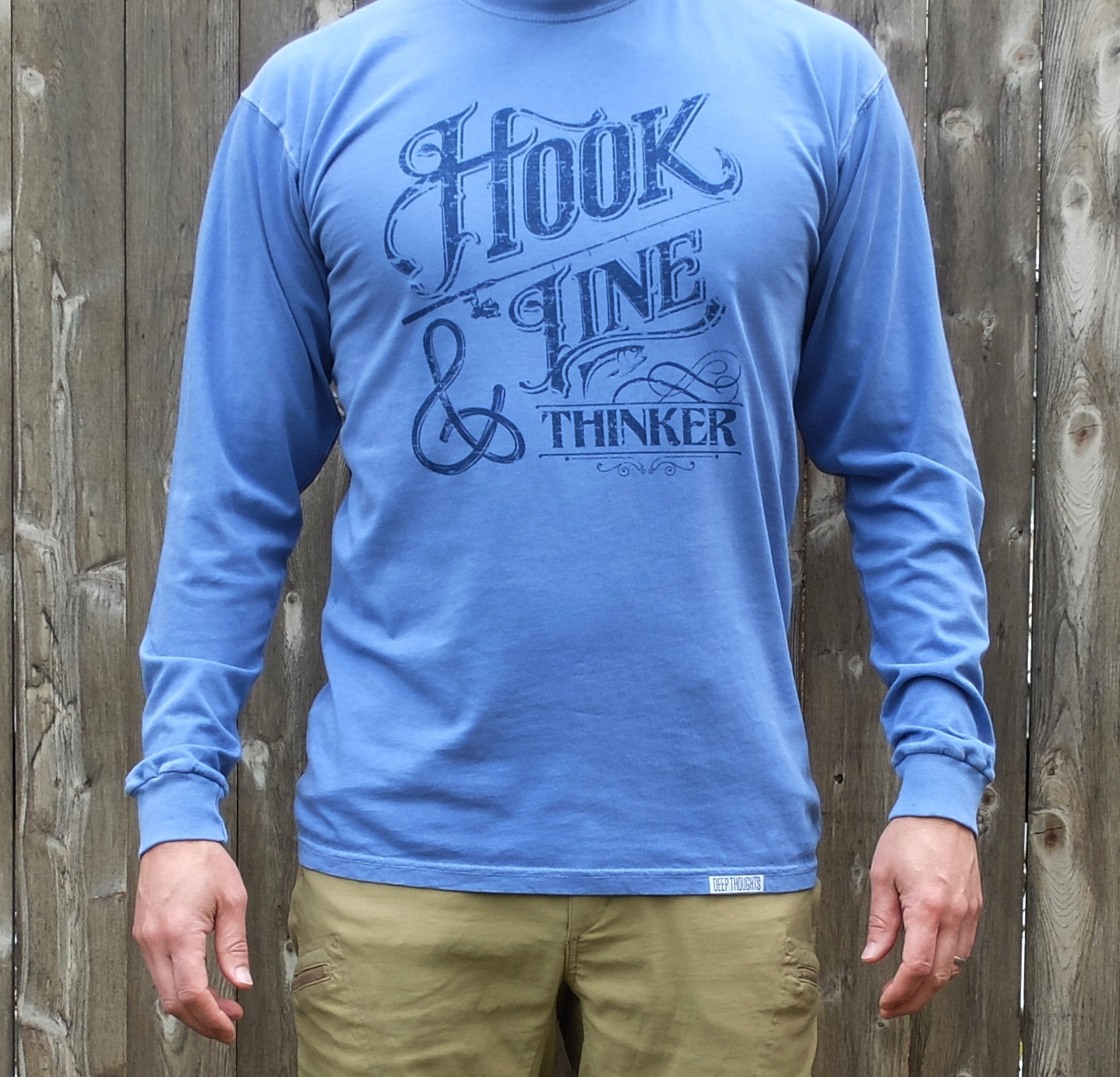 man wearing washed periwinkle blue long sleeve cotton t-shirt with navy blue hook line and thinker fishing graphic
