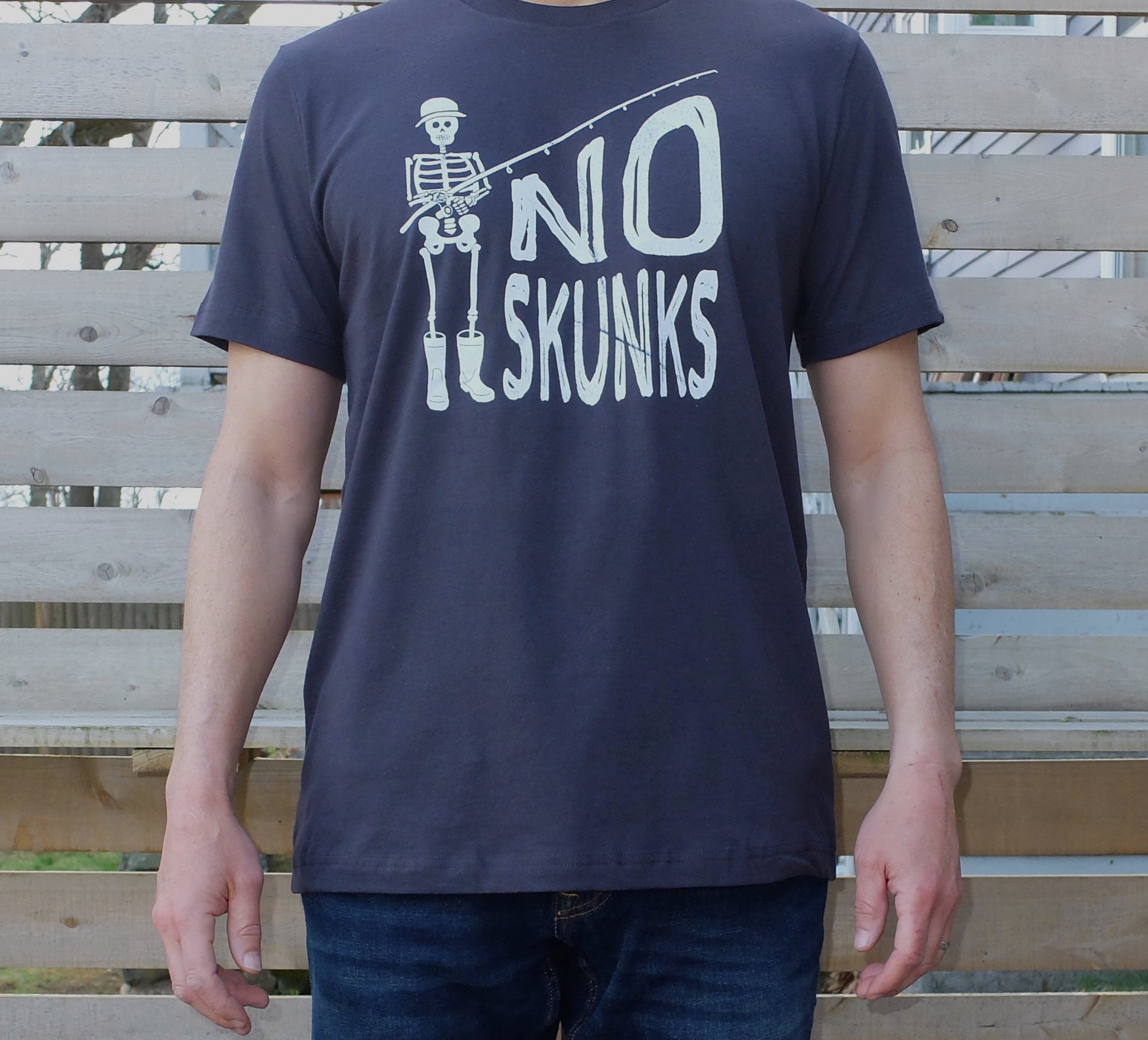 man wearing dark grey cotton t-shirt with white skeleton fisherman graphic and No Skunks text