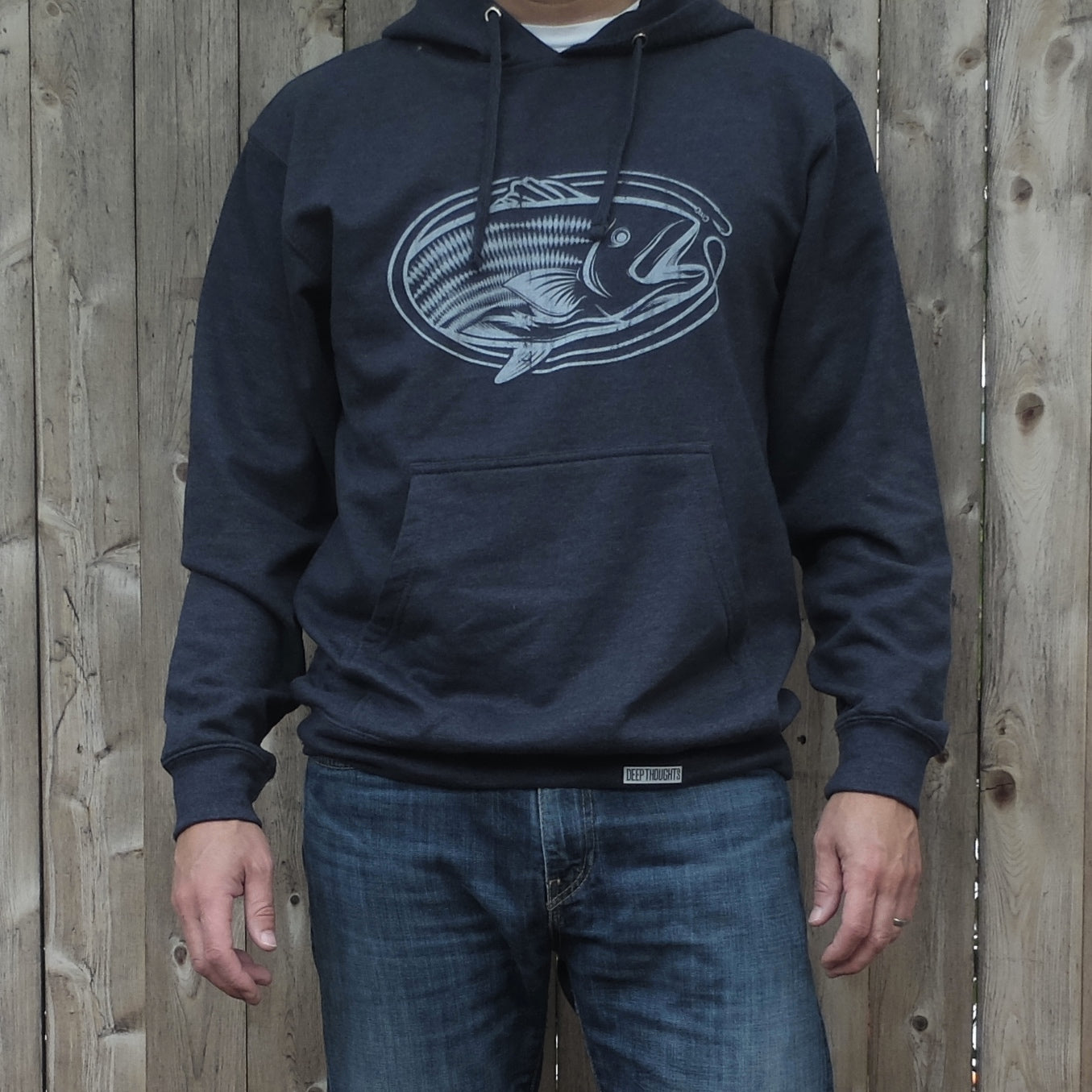 man wearing heather navy blue hoodie with vintage style white oval-shaped striped bass fishing graphic