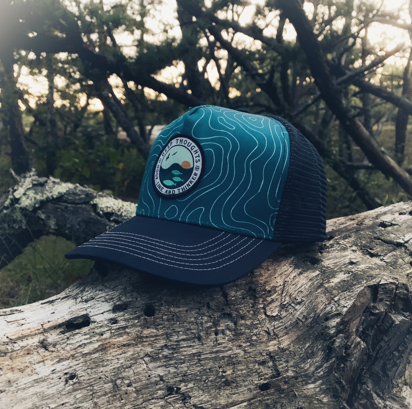 aquamarine and navy blue trucker hat with round patch depicting ocean swells with fish beneath the waves