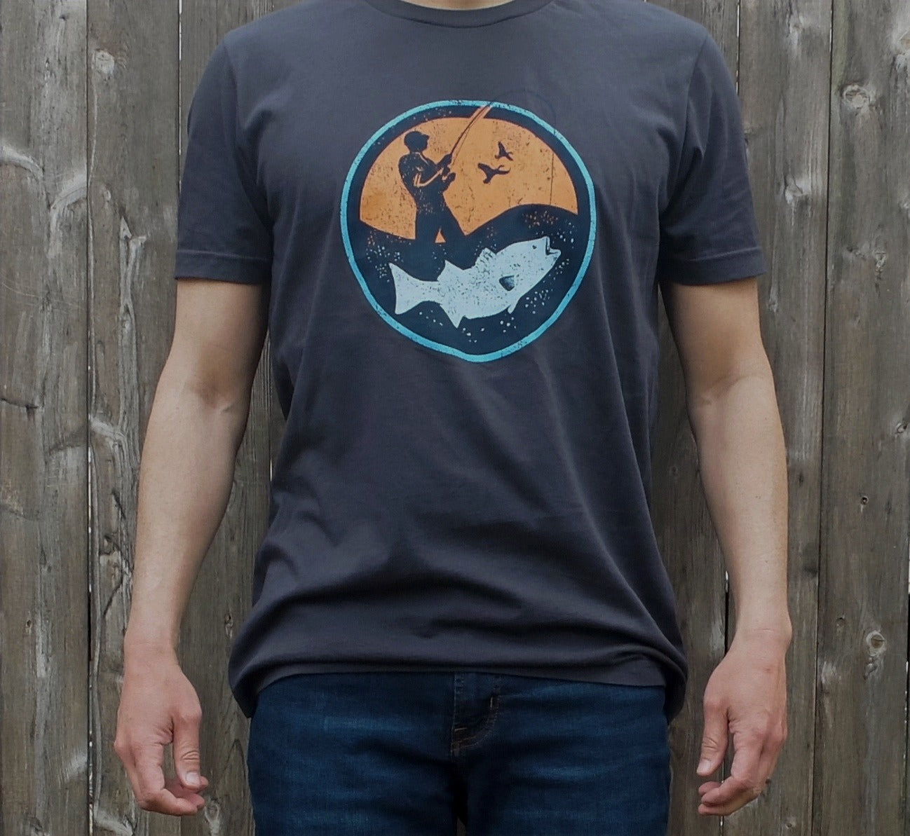 man wearing dark grey cotton t-shirt with round orange and blue surf fisherman logo