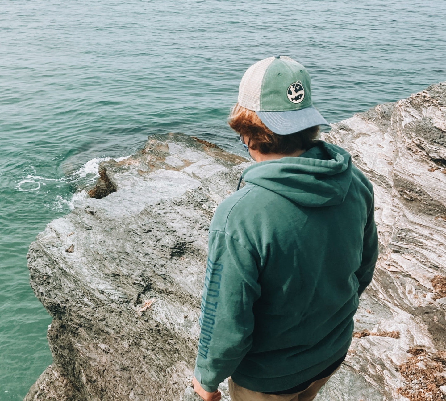 man wearing Deep Thoughts blue green and sand colored trucker cap by the ocean