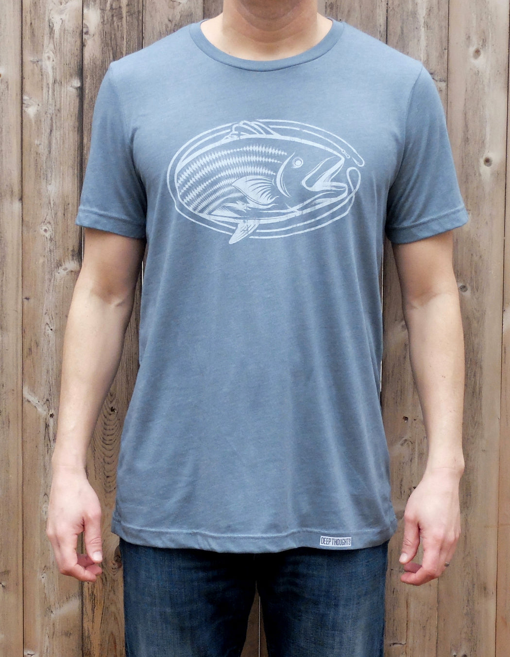 man wearing heather slate blue t-shirt with white oval-shaped striped bass fishing graphic