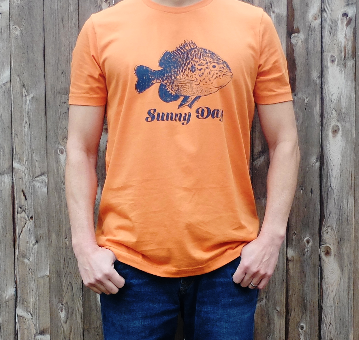 man wearing burnt orange cotton t-shirt with navy colored bluegill and Sunny Day text